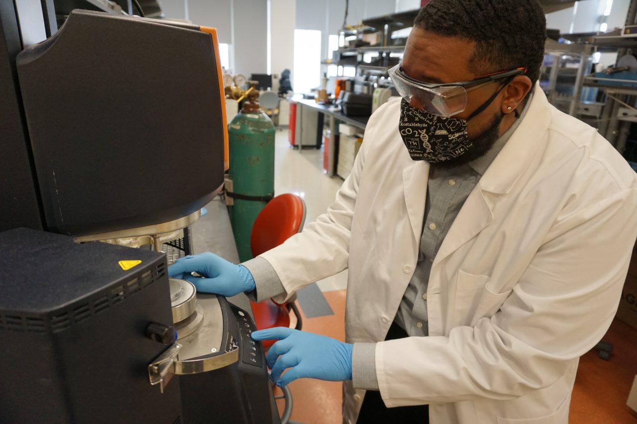 A man in a lab coat and protective gloves adjusts a laboratory instrument