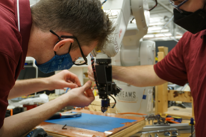Two people make adjustments to the arm of a 3D printer. 