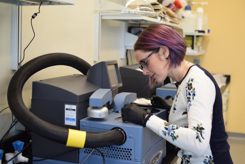 A woman with purple hair works with an instrument in a lab.